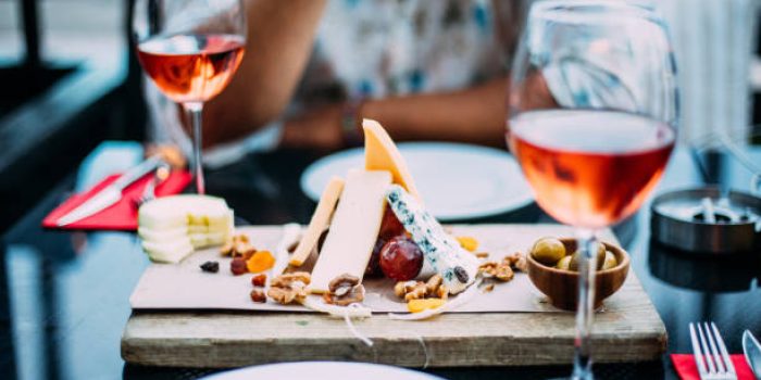 wo glasses of rose wine and board with fruits, bread and cheese on wooden table